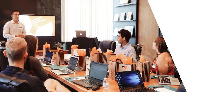 Mann steht vor Leuten, die neben einem Tisch mit Laptops sitzen